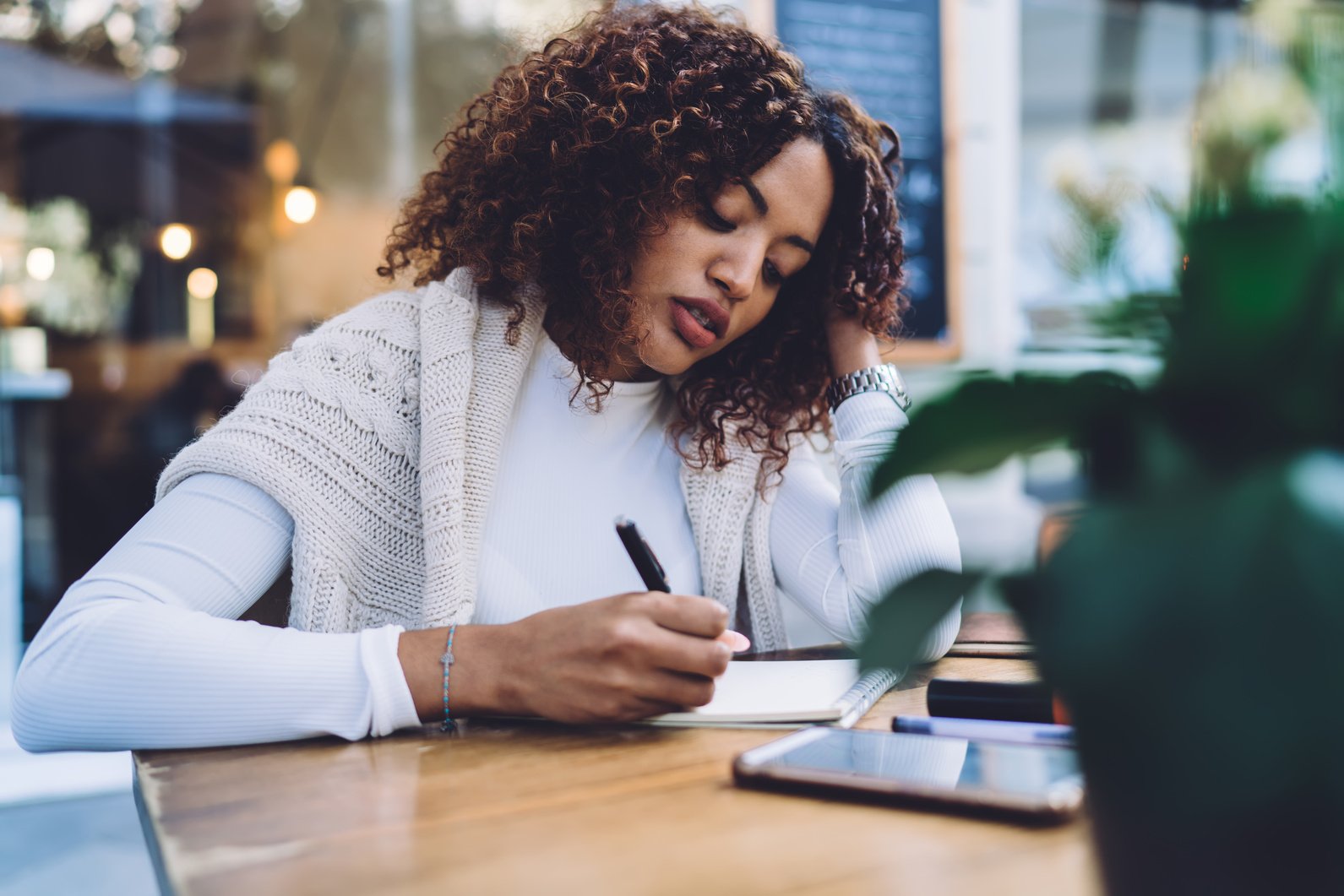 Focused ethnic woman writing in planner